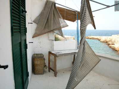 Sulla destra si dirama un�ulteriore scala che porta a un�abitazione totalmente dipinta di bianco, sul cui terrazzino si trovano un tavolino in legno logorato dalle intemperie e dalla salsedine e un cestino in vimini sui cui volteggia lo scheletro di una tenda spinta dal vento